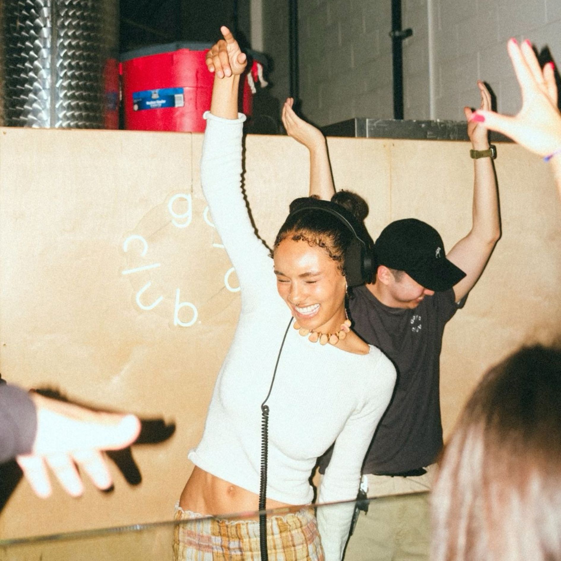 DJane mit Kopfhörern tanzt lachend hinter dem DJ-Pult